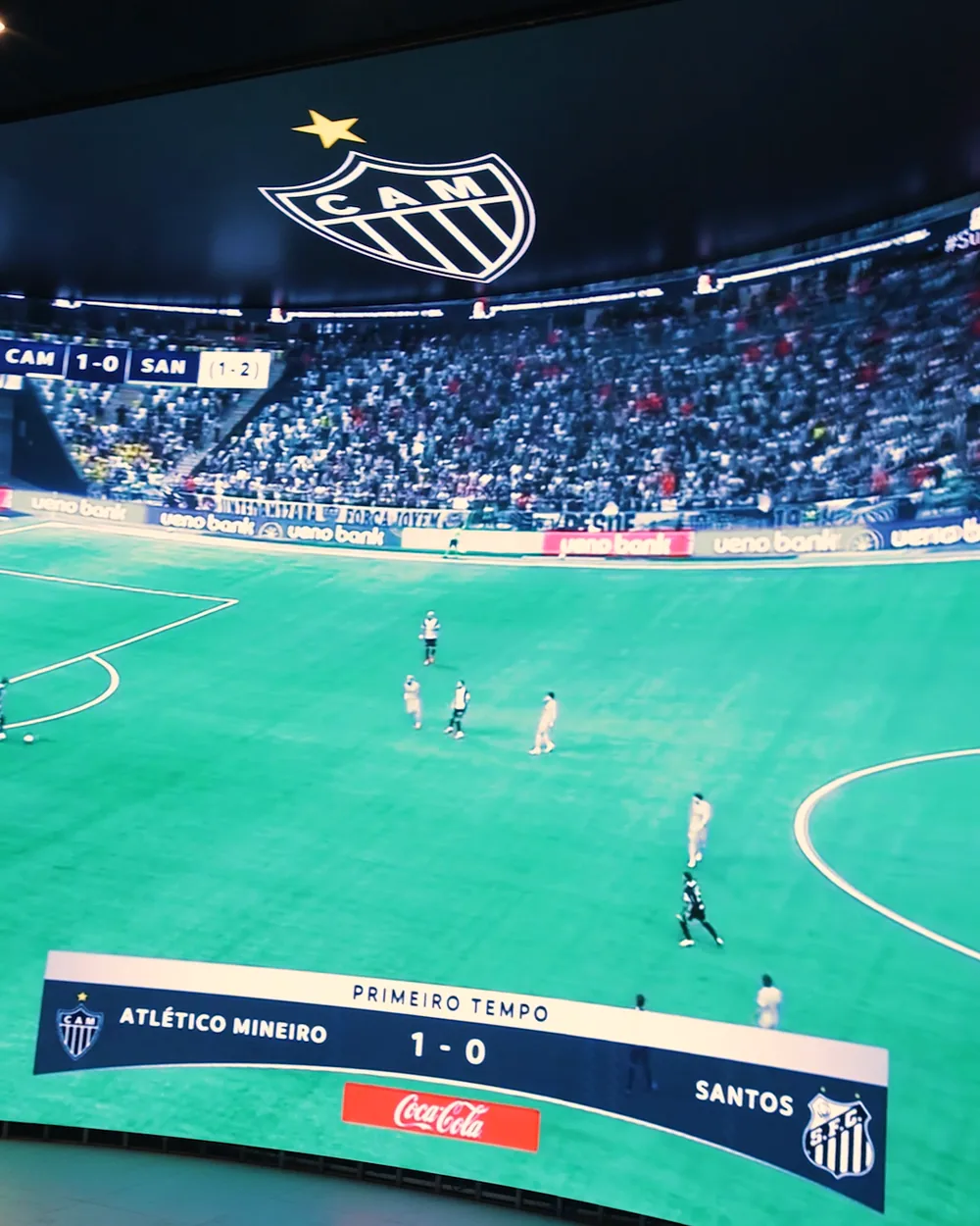 Painel de LED curvo do Bar da Massa transmitindo jogo do Atlético Mineiro, com o escudo do Galo acima do campo