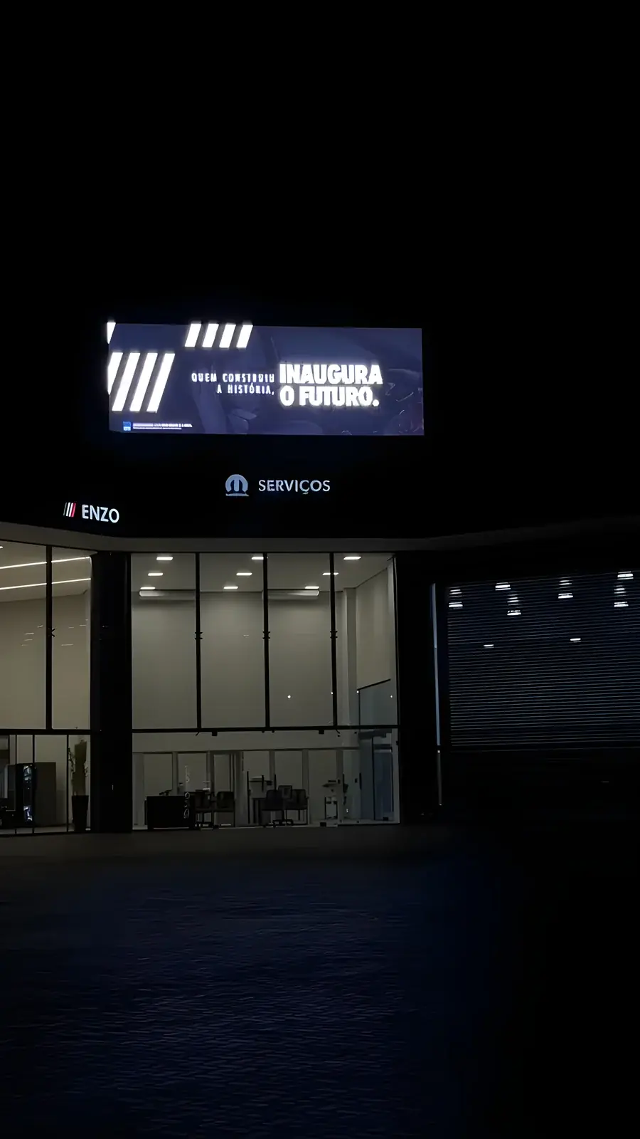 Fachada da Fiat Campo Grande à noite com painel de LED exibindo comunicação institucional